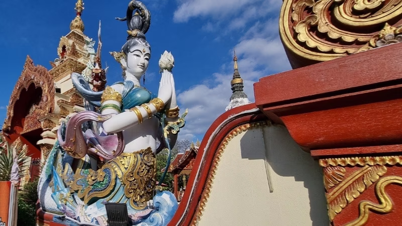 Australians retiring in Thailand Deity statue beside ornate temple architecture under blue sky in Thailand