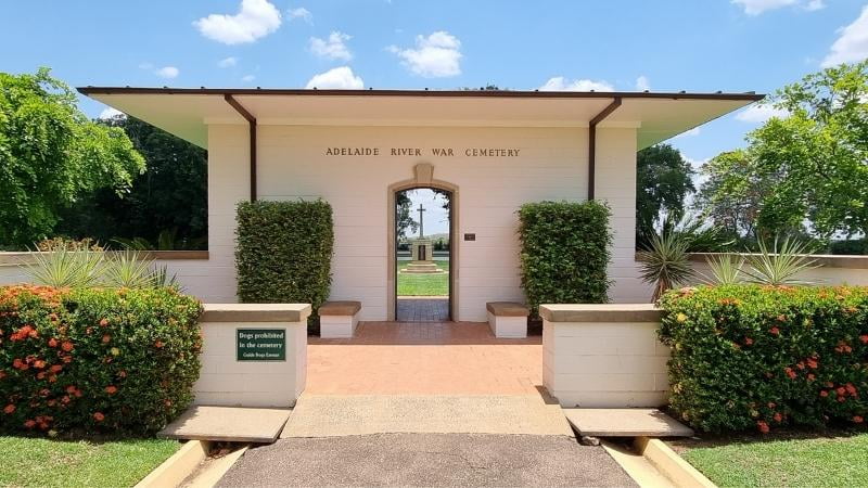 Darwin to Cairns road trip Entrance to Adelaide River War Cemetery in the Northern Territory, featuring manicured gardens, memorial archway and a central cross visible through the gate