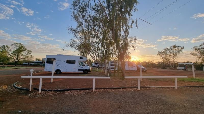 Darwin to Cairns road trip Motorhomes parked at a red dirt caravan site at Threeways Caraven Park, with gum trees and sunrise in the outback sky
