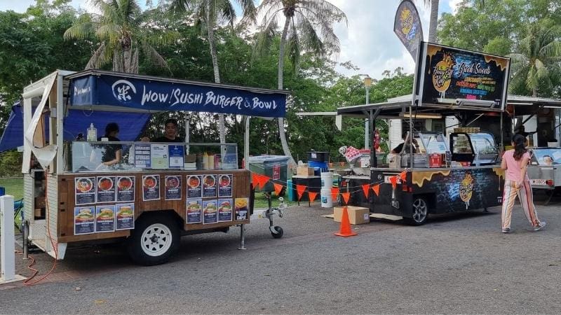 Darwin to Cairns road trip Food trucks serving sushi burgers and desserts at Mindil Beach Sunset Markets, with palm trees and visitors in the background