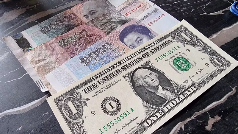 Stack of international banknotes including US dollar and Cambodian Riel displayed on a dark marble surface