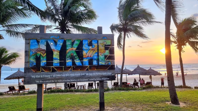 Long Stays in Vietnam Colourful My Khe Beach sign with palm trees and straw umbrellas along the Da Nang coastline at sunrise