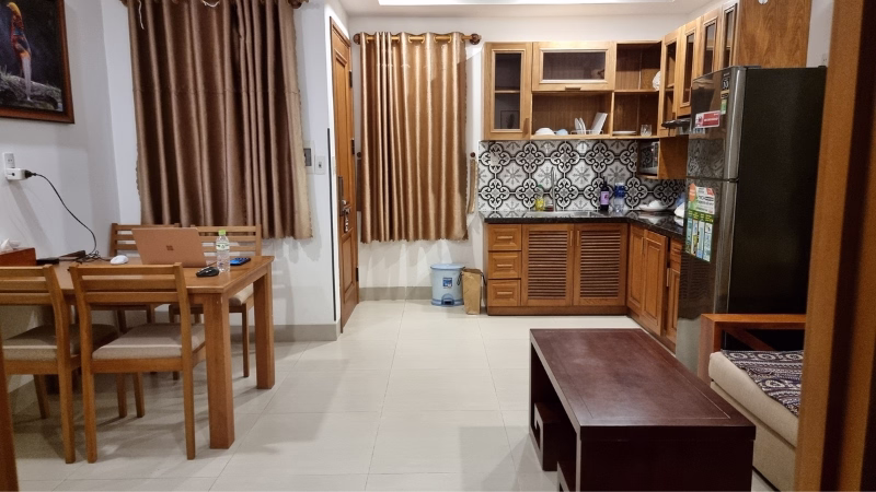 Compact apartment kitchen and dining area with wooden furniture, patterned tile backsplash, and stainless steel fridge in Da Nang