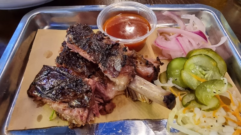 Long Stays in Vietnam Smoked beef ribs served with barbecue sauce, pickles and onions on a metal tray at a restaurant in Da Nang, Vietnam