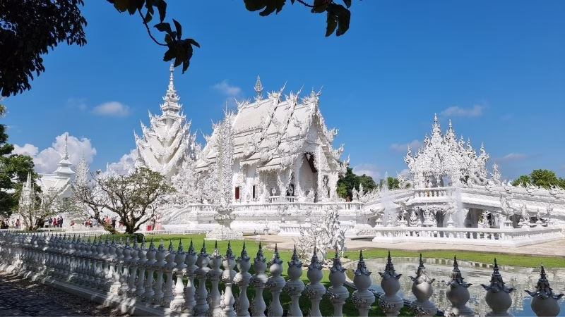 White Temple (Wat Rong Khun) in Chiang Rai featuring intricate white carvings, mirrored details and clear blue skies above the ornate Thai architecture