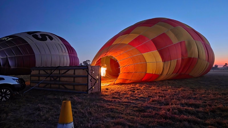 Hot air balloon being inflated with flames at dawn in the field, preparing for a sunrise flight over the Scenic Rim South East QLD