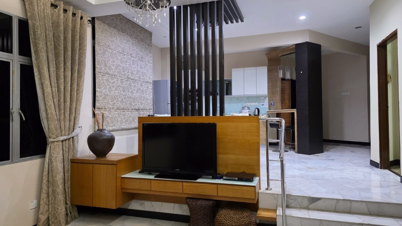 Modern open-plan living room in our long stay Penang, Malaysia apartment with TV unit, marble flooring, decorative partition, and view into a contemporary kitchen with bar counter